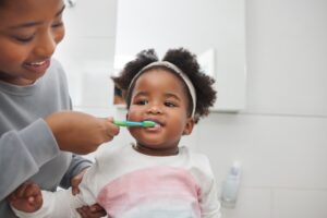 Mother helping brush her toddler's teeth properly