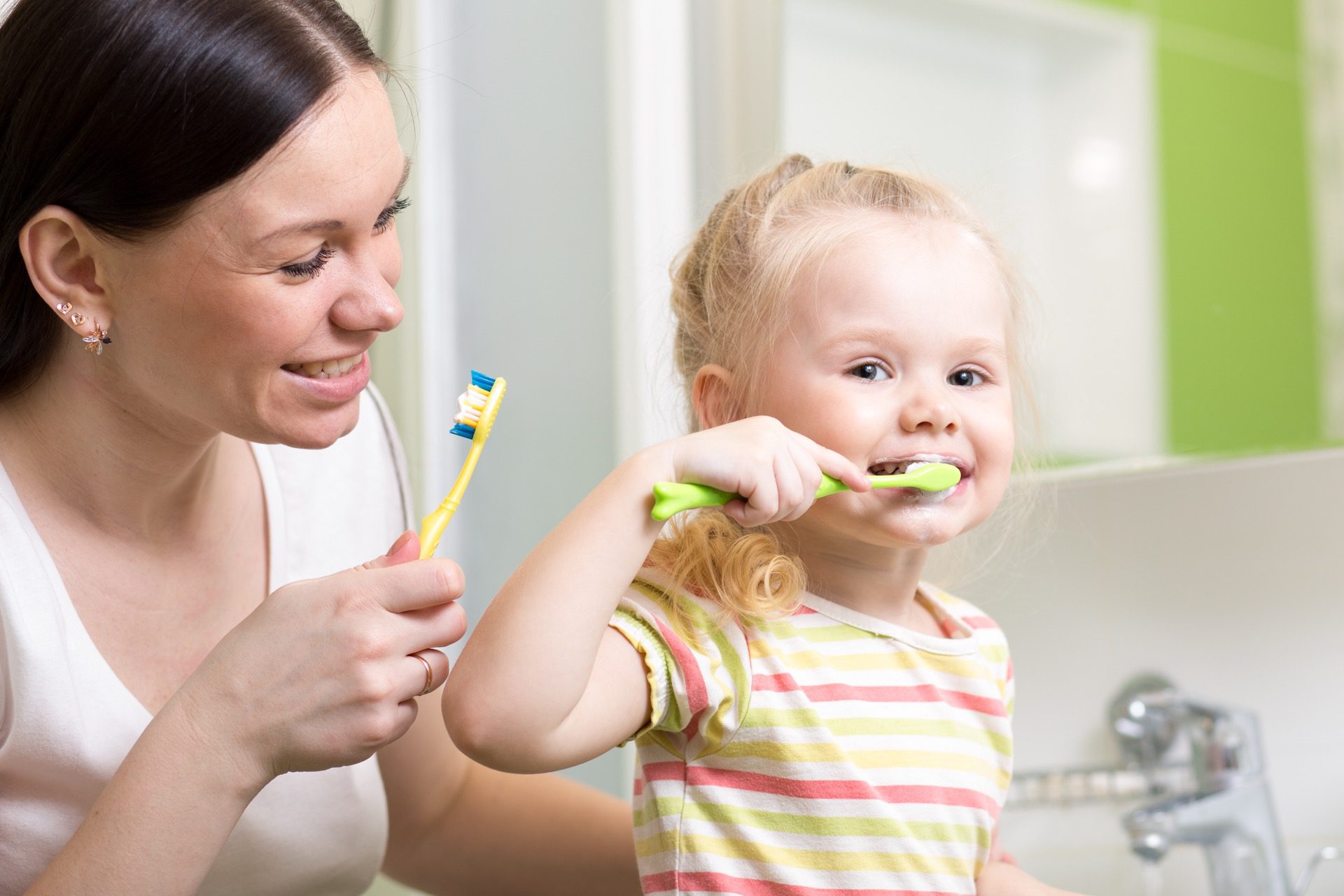 Mother teaching toddler how to brush teeth after noticing white spots on her toddler's teeth